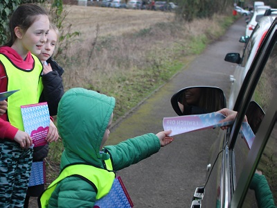 Jude hands an anti-idling leaflet to a driver watched on by two fellow students