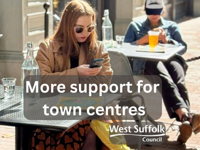The image shows a woman at a table outside a cafe or restaurant. She has a bottle of drink on her table with a glass and is looking on her mobile phone. The text reads "More support for town centres" The West Suffolk Council logo features icon
