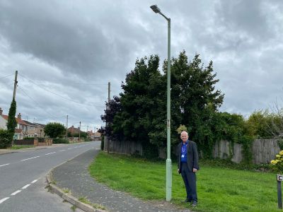Image of Cllr Gerald Kelly in front of a newly converted streetlight icon